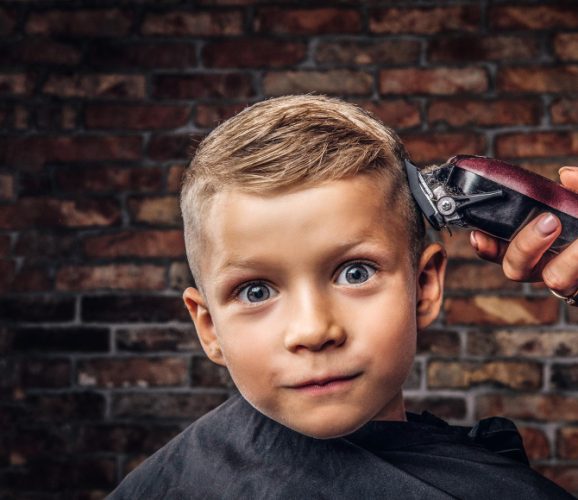 close-up-portrait-cute-smiling-boy-getting-haircut-against-brick-wall